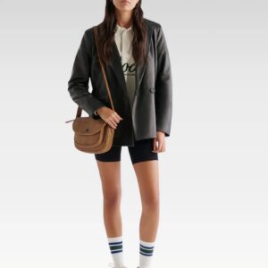 Model wearing the women’s black leather double breasted blazer styled over a white blouse and shorts, showcasing a modern city-chic look with functional front pockets.